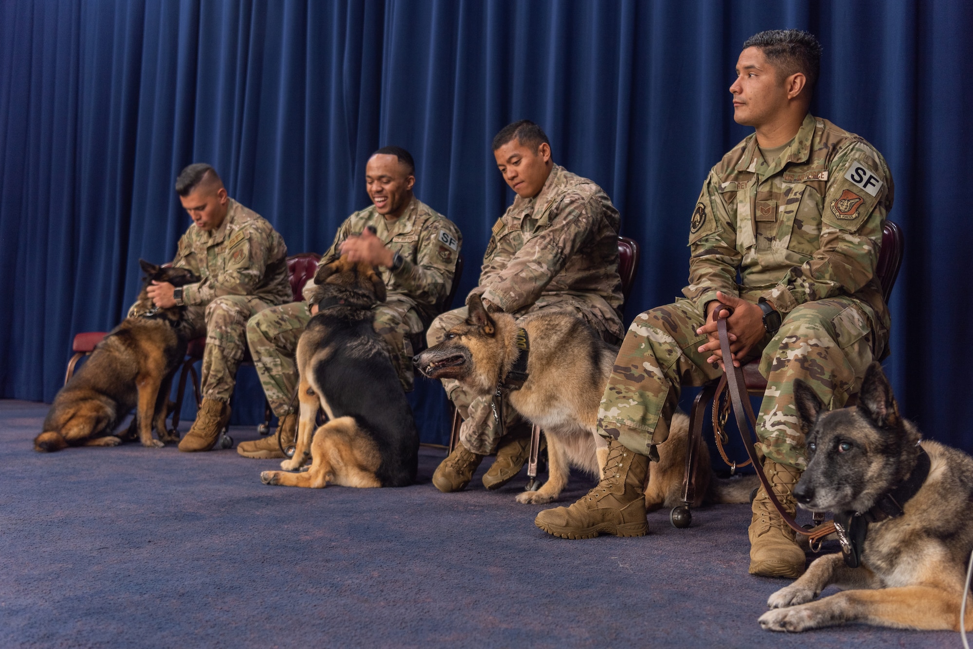 U.S. Air Force military working dog (MWD) handlers assigned to the 18th Security Forces Squadron sit by their MWDs during a MWD retirement ceremony July 26, 2019, on Kadena Air Base, Japan. MWDs and their handlers must have trust and patience with one another to work together as a team and accomplish the mission safely and effectively. (U.S. Air Force photo by Senior Airman Cynthia Belío)