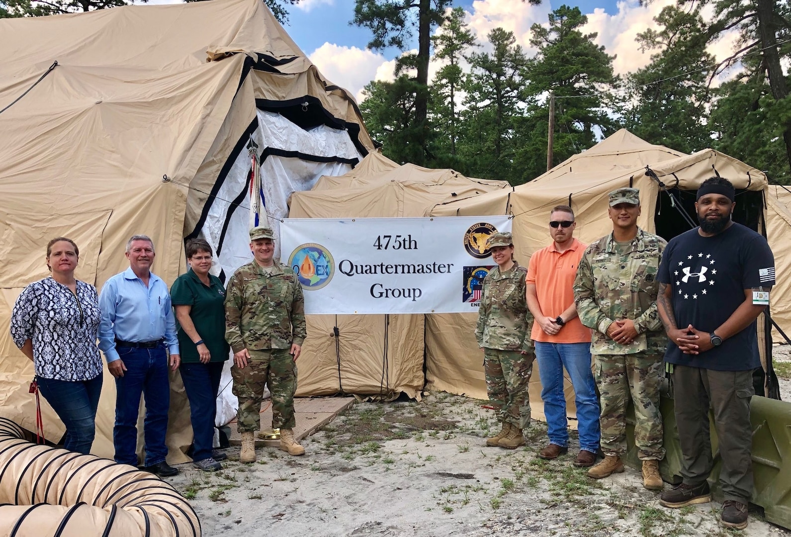 military and civilian personnel stand outside a tent