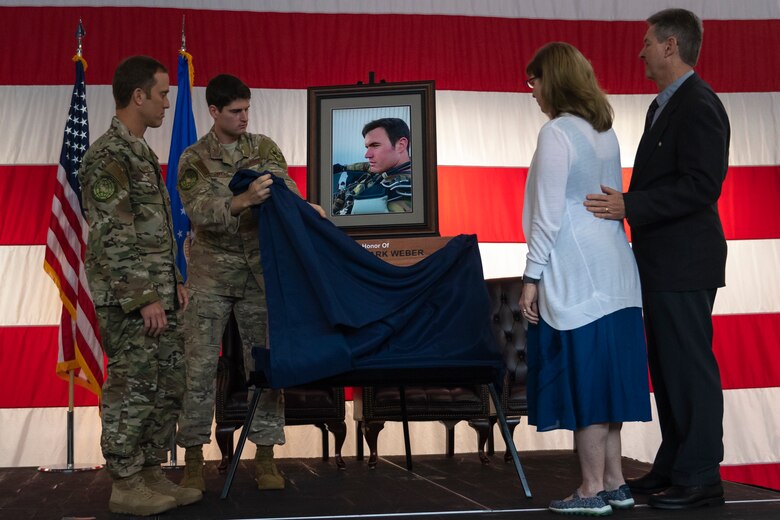 Airmen from the 38th Rescue Squadron (RQS), left, unveil a photo and inscription honoring Capt. Mark Weber, during a dedication ceremony Aug. 16, 2019, at Moody Air Force Base, Ga. The event room in building 400 at Moody was dedicated to and renamed in honor of Capt. Mark Weber, 38th RQS combat rescue officer. Weber, a Texas native, was killed in an HH-60G Pave Hawk crash in Anbar Province, Iraq, March 15, 2018, while supporting Operation Inherent Resolve. (U.S. Air Force photo by Airman 1st Class Taryn Butler)