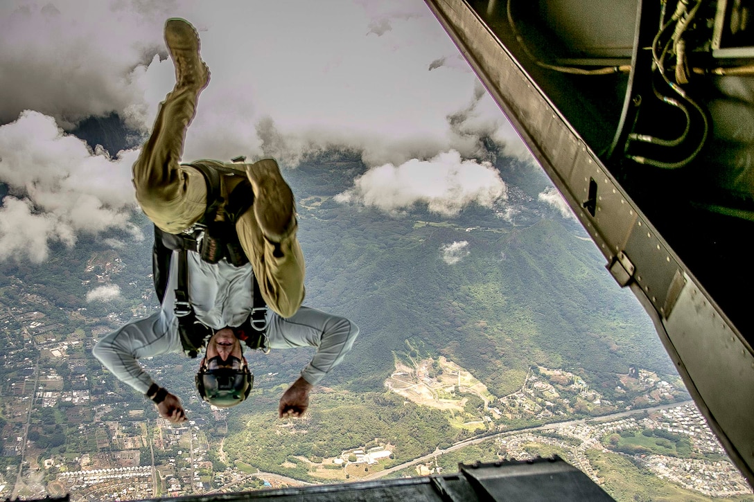 A service member jumps out of an aircraft upside down.