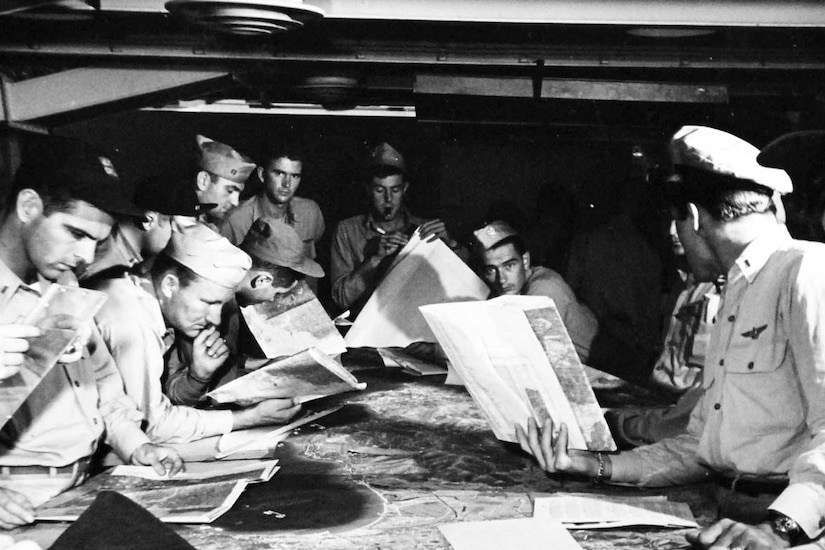 Men look at documents on a table.