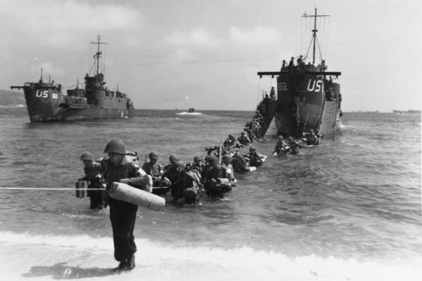 Soldiers wade from ship to beach.