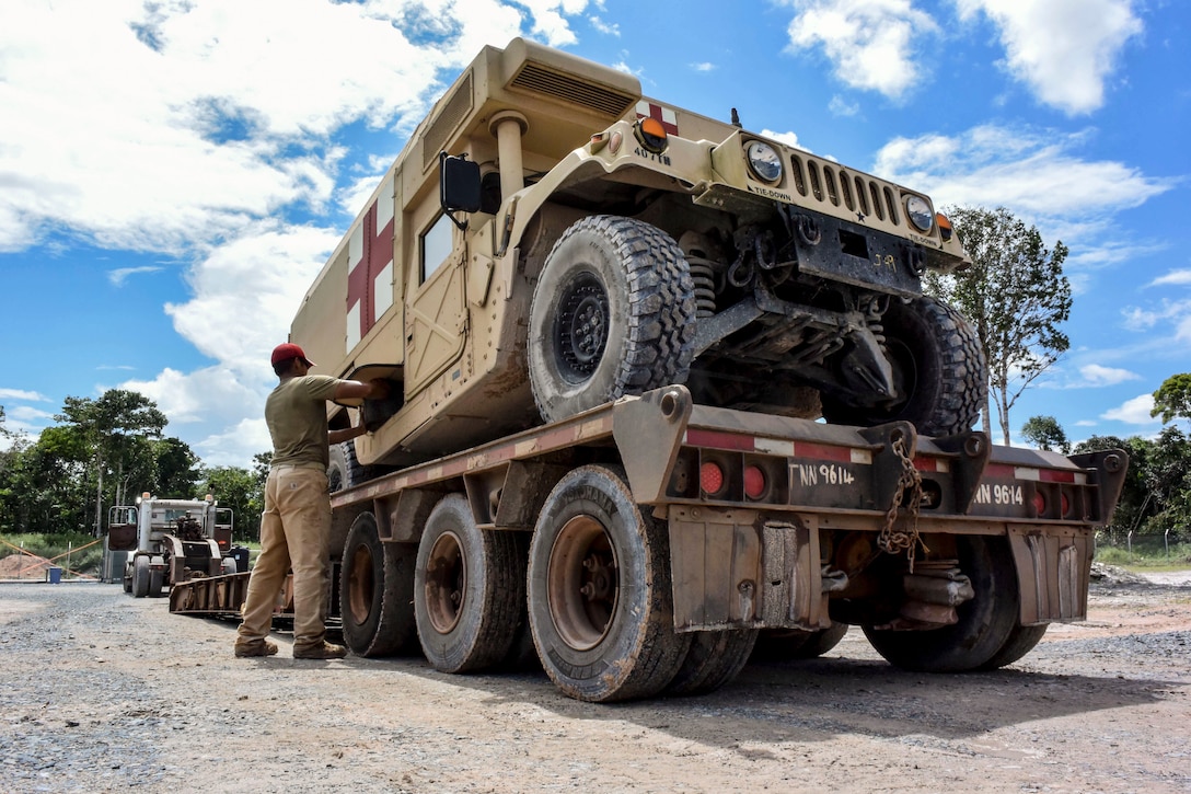 An airman works on a Humvee sitting atop a wheeled platform.