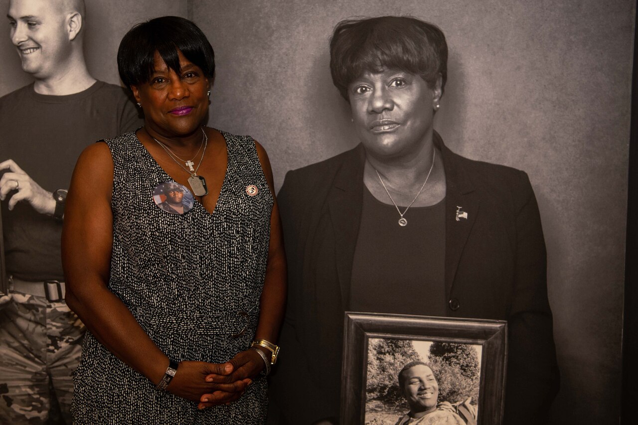 A woman poses next to a black and white photo of herself.