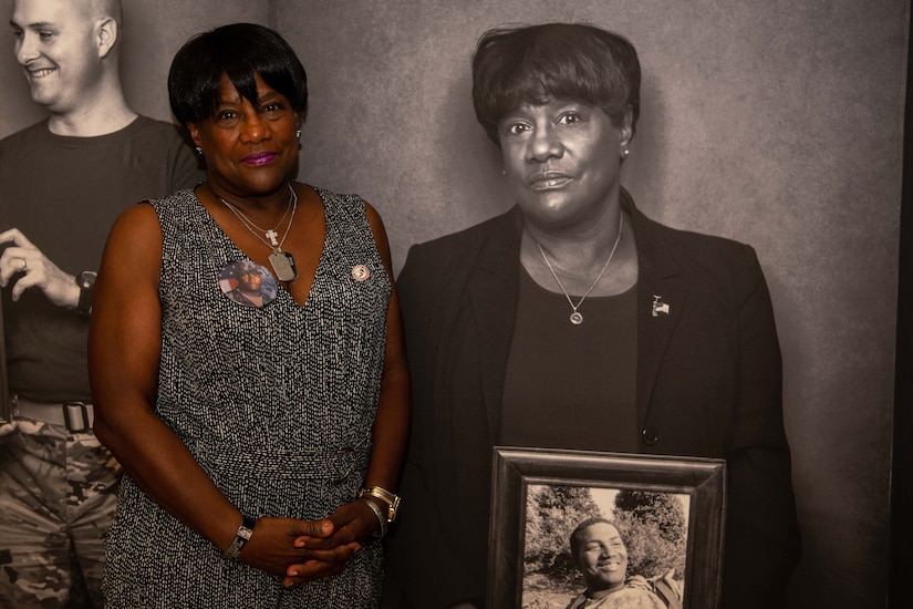 A woman poses next to a black and white photo of herself.