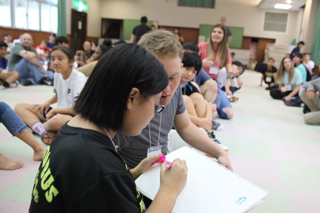 伝言ゲームで、伝わってきた言葉を書く中学生。名護市教育委員会主催の市内中学生を対象にした英語体験学習が名護青少年の家で開催され、米海兵隊基地司令官や海兵隊員やその家族、日本人ボランティアら大勢参加し、楽しく英会話を体験しました。