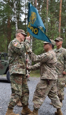 Col. Christopher Varhola passes the 2500th Digital Liaison Detchment colors to Brig. Gen. Michael T. Harvey symbolizing his relinquishment of command during a change of command ceremony Aug. 17 at Camp Normandy, Grafenwoehr, Germany. After three years in the position, Varhola passed command of the 2500th DLD to Col. Gregory Gimenez.