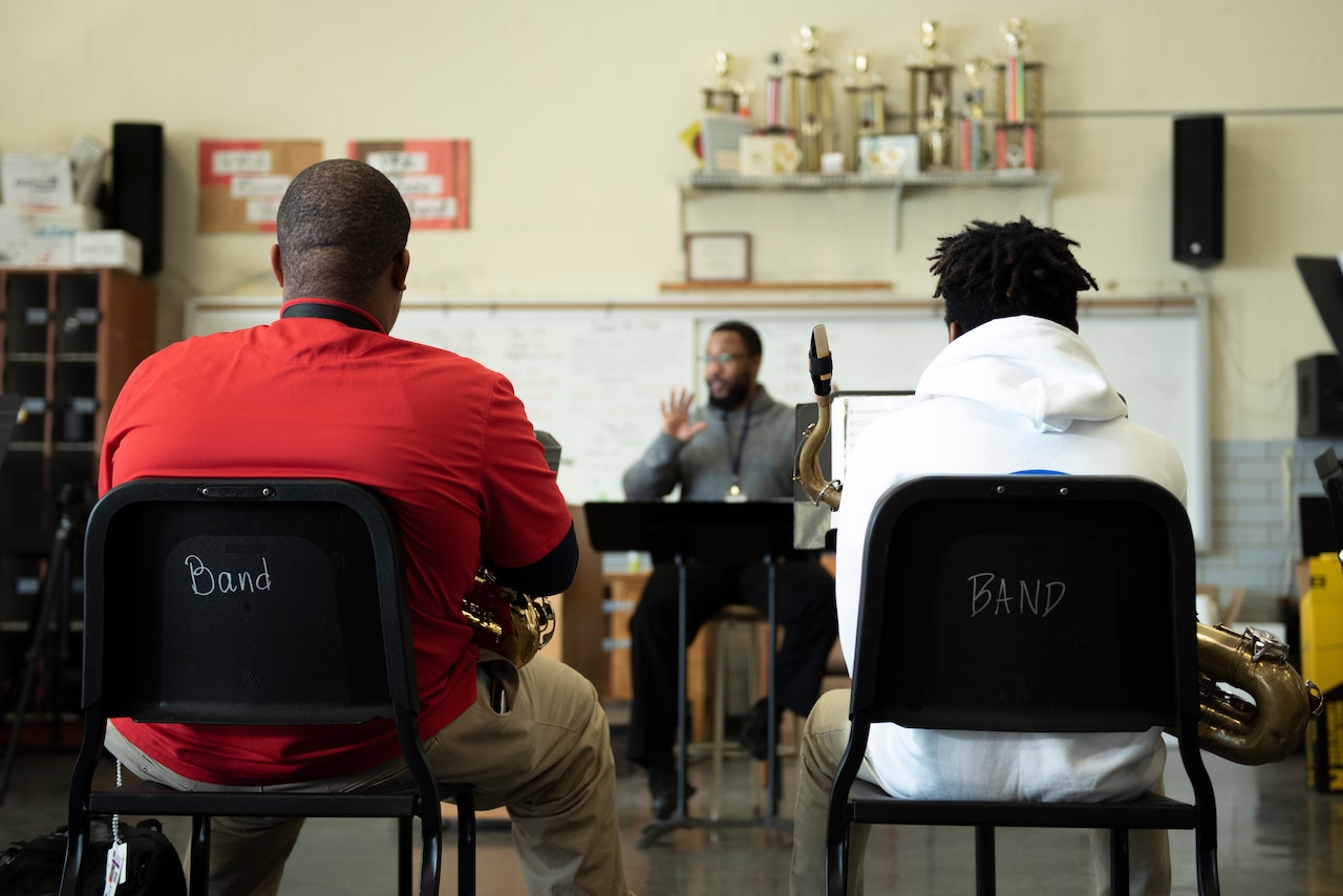 A teacher seen through two students sitting with their backs to the camera.