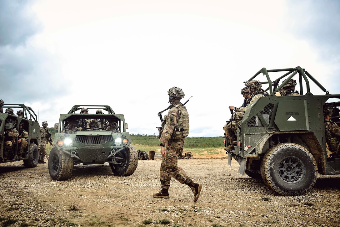 A soldier walks alongside soldiers riding in military vehicles.