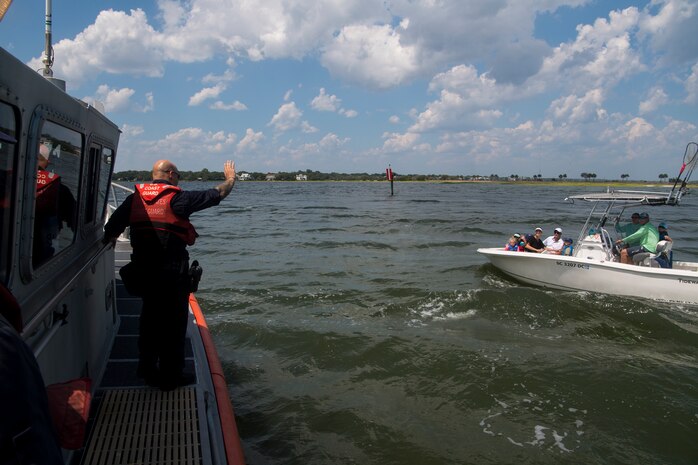 U.S. Coast Guard Petty Officer 2nd Class James Sokol, a maritime enforcement specialist assigned to USCG Station Charleston, signals an approaching vessel while performing inspections in support of Operation SHRIMP and GRITS in Charleston Harbor, August 9, 2019. Operation SHRIMP and GRITS is an annual multi-jurisdiction and multi-state maritime  law enforcement operation that promotes safety to recreational and commercial boaters traveling along the water across South Carolina, North Carolina, Georgia and Florida. Approximately 104 different agencies in the four states participated in the operation with the U.S. Coast Guard, covering about 500 miles of coastline.