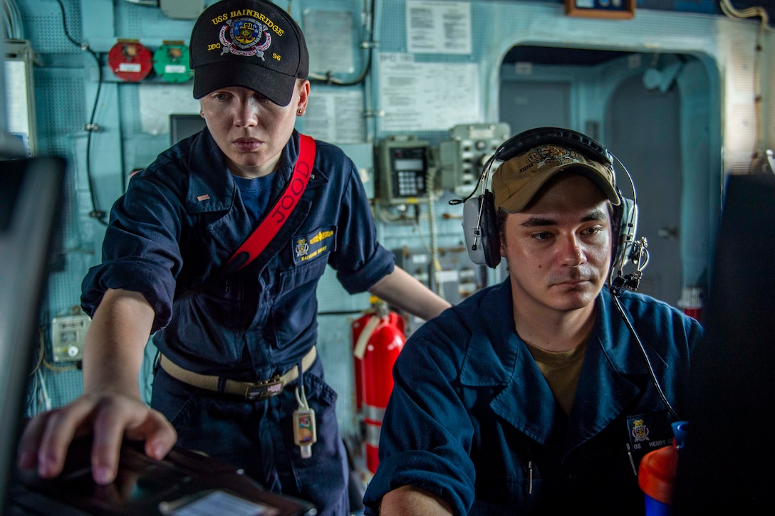 One sailor stands while sailor sits, both looking forward.