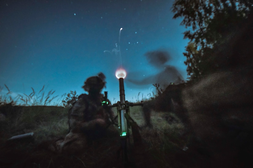 Soldiers fire a military weapon at night.