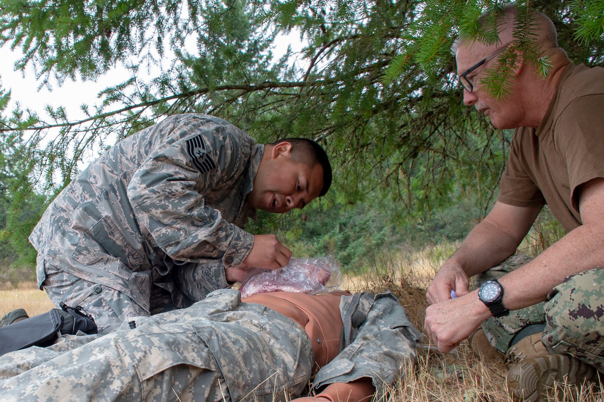 Chief Hospital Corpsman Sammy Willis, an instructor assigned to Navy Reserve Navy Medicine Education and Training Command, evaluates U.S. Air Force Tech Sgt. Jose Chaires tending to a simulated casualty during a tactical combat casualty care (TCCC) class for exercise Tropic Halo 2019 at Joint Base Lewis-McChord in Tacoma, Wash., Aug. 7, 2019. Tropic Halo is designed to enhance Operational Hospital Support Unit Bremerton's medical and mission capabilities on several levels: increase TCCC and trauma nurse core course readiness rates while minimizing overall training costs; promote intra-service cohesion with collaborative training in a joint service environment and leverage Navy and Air Force command assets to generate better training opportunities. (U.S. Navy photo by Mass Communication Specialist 1st Class Ryan Riley)