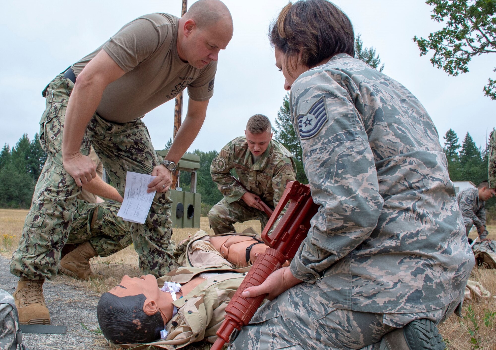 Hospital Corpsman 1st Class Rob Johnston, an instructor assigned to Navy Reserve Navy Medicine Education and Training Command and selected for the rank of chief, evaluates U.S. Air Force Tech Sgt. Kristin Trujeque tending to a simulated casualty during a tactical combat casualty care (TCCC) class for exercise Tropic Halo 2019 at Joint Base Lewis-McChord in Tacoma, Wash., Aug. 7, 2019. Tropic Halo is designed to enhance Operational Hospital Support Unit Bremerton's medical and mission capabilities on several levels: increase TCCC and trauma nurse core course readiness rates while minimizing overall training costs; promote intra-service cohesion with collaborative training in a joint service environment and leverage Navy and Air Force command assets to generate better training opportunities. (U.S. Navy photo by Mass Communication Specialist 1st Class Ryan Riley)