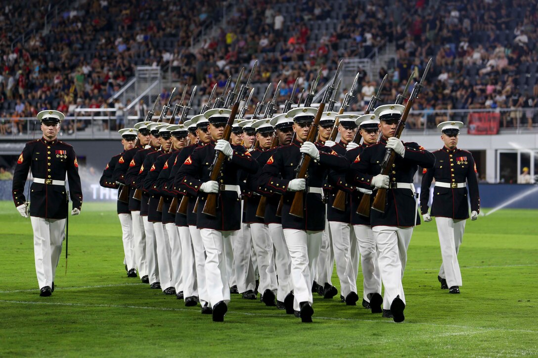 A group of Marines march together in a sports stadium.