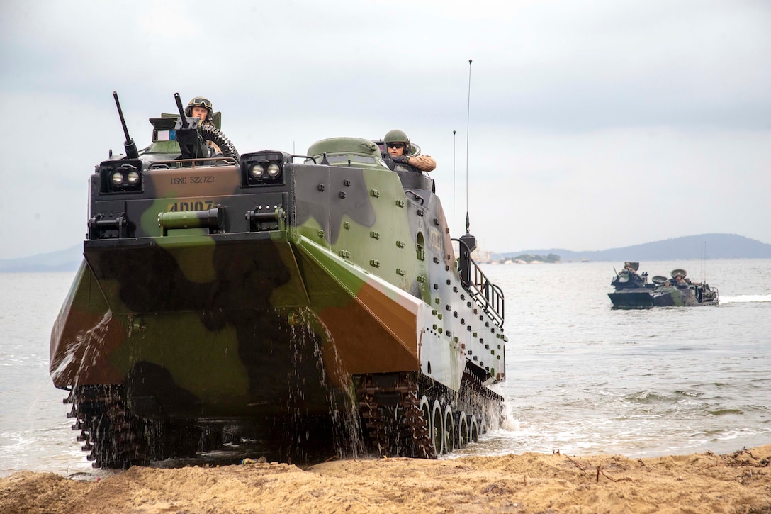 Marines ride in military vehicles on a beach.