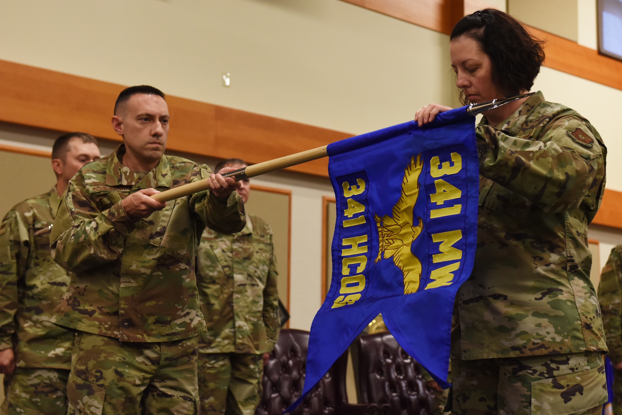 Lt. Col. Stephen Boglarski, 341st Healthcare Operations Squadron commander, left, and Master Sergeant Kimberly Severyn, 341st HCOS superintendent, unfurl the HCOS guidon August 16, 2019, at the Grizzly Bend on Malmstrom Air Force Base, Mont.