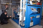 A.J. Ballard, the energy manager for the Maine Army National Guard points out some of the engine details of the award-winning combined heat and power system at the Maine Army National Guard Army Aviation Support Facility in Bangor, Maine. "This is a wonderful machine," said Ballard. "This system produces electricity we don't have to pay for, and heat we don't have to pay for."