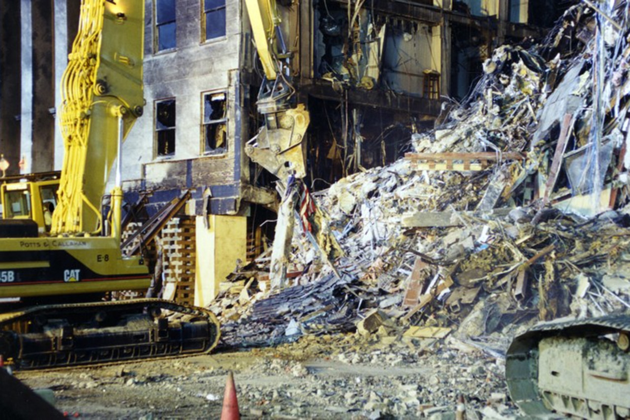 A large machine picks up debris, including an American flag.