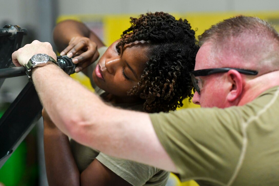 Two airmen use tools to work on military equipment.