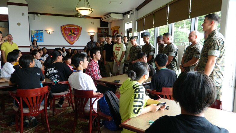 高校生のための夏季英語クラスにボランティアで集まった海兵隊員を高校生たちに紹介。沖縄県うるま市役所と米海兵隊基地キャンプ・コートニーの交流事業の一環で、市内の高校生を対象にした夏季英語クラスが月曜日に始まり、基地内で行われるクラスで１週間を通して高校生たちのコミュニケーション能力の向上を図ります。