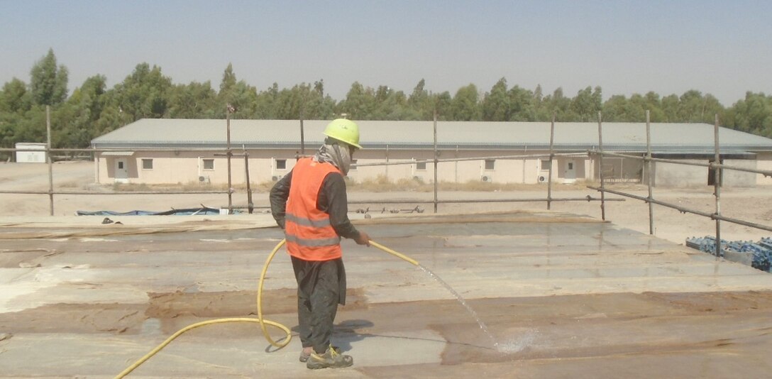 Local National employee sprays water in the curing process of the concrete roof slab.
