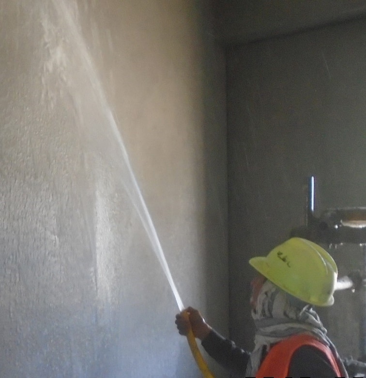 A LNQA sprays water on the interior plaster of the buildings being constructed at the Aviation Enhancement Life Support Area.