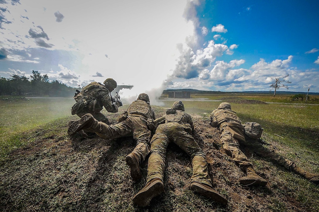 Four soldiers lie on the ground firing their weapons.