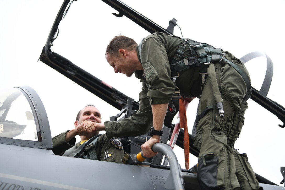 U.S. Air Force Staff Sgt. Derreck Day, 48th Operations Support Squadron Survival, Evasion, Resistance and Escape specialist, shakes the hand of U.S. Air Force Capt. Caleb Wyatt, 493rd Fighter Squadron F-15C Eagle electronic combat pilot, after a familiarization orientation flight at Royal Air Force Lakenheath, England, Aug. 16, 2019. Due to the nature of military service, this is the first duty station the pair have shared at the same time since beginning their Air Force journey. (U. S. Air Force photo by Airman 1st Class Shanice Williams-Jones)