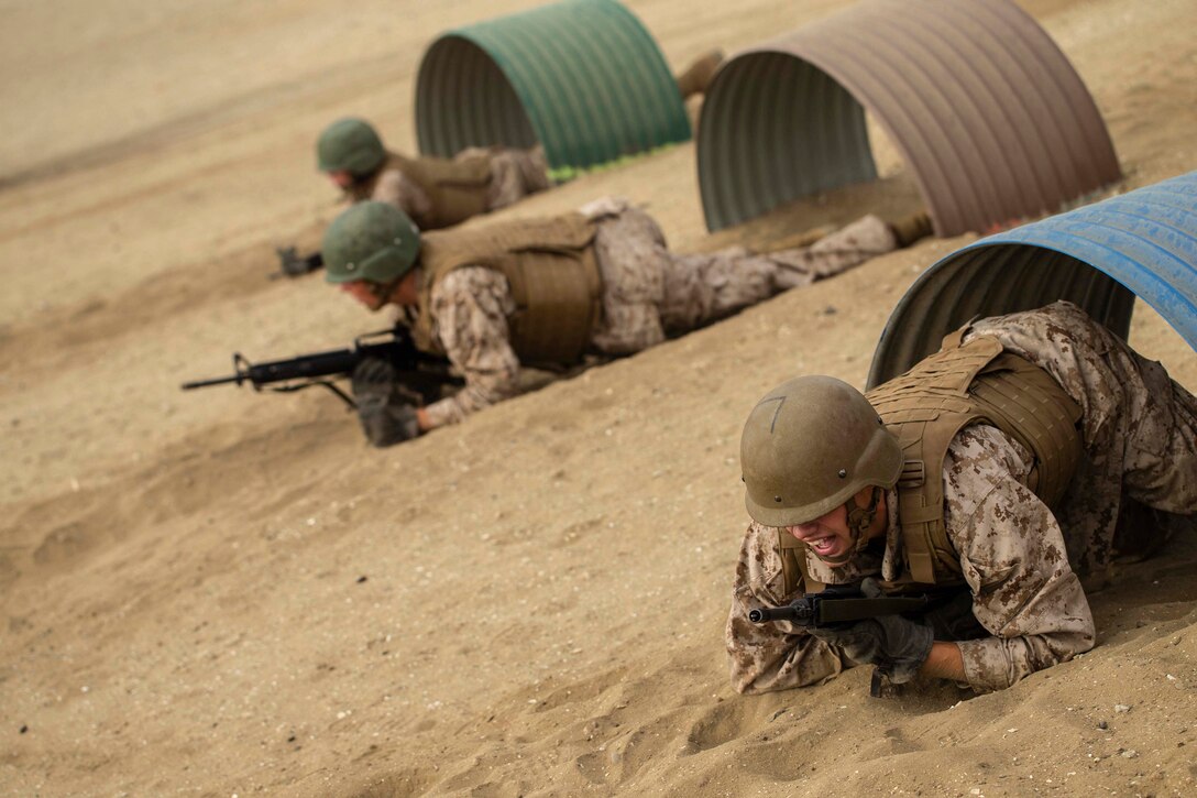 Three service members crawl under an obstacle.