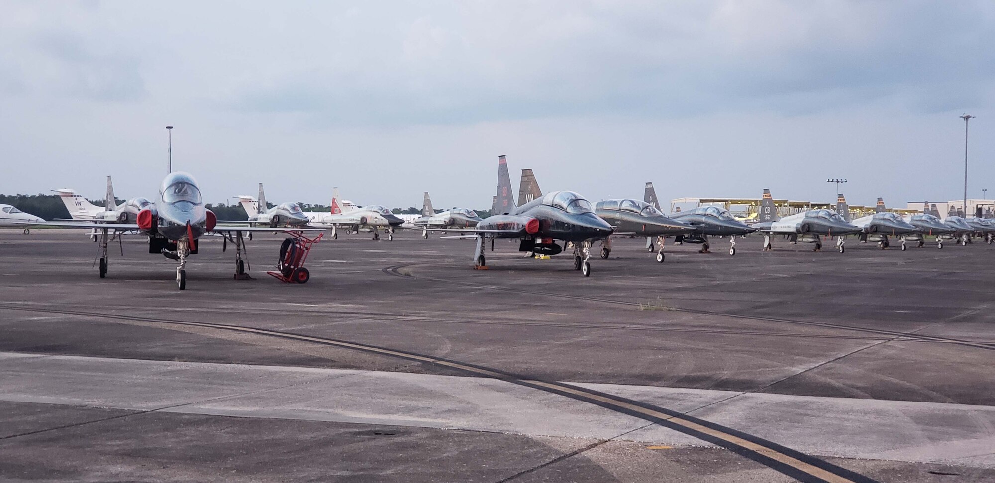 A row of parked T-38 Talon aircraft in the foreground and a row of T-1 Jayhawk aircraft in the background sit on the ramp at Naval Air Station Fort Worth Joint Reserve Base, New Orleans, Aug. 9, 2019, during FAIP Flag. Instructor pilots from all over the country fly in to participate in the event, including pilots who have moved on from being instructor pilots. (U.S. Air Force photo by Capt. Gared Chapman)