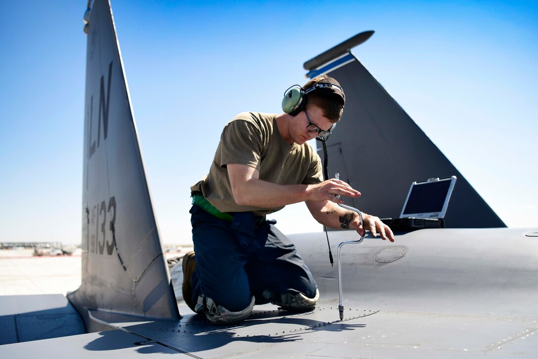 An airman uses a tool to screw a panel shut.