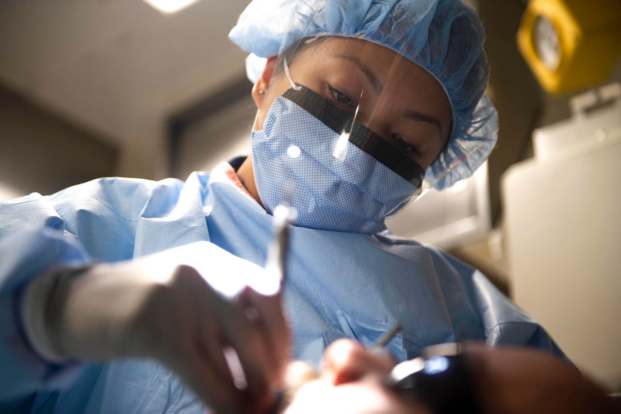 A sailor uses tools to clean a patient's teeth.