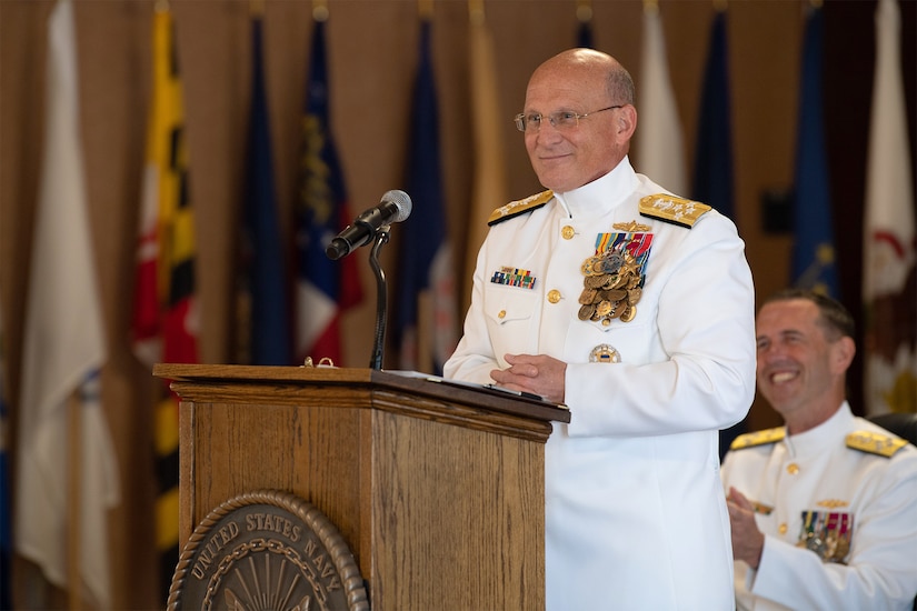 Admiral in white dress uniform speaks at a lectern.