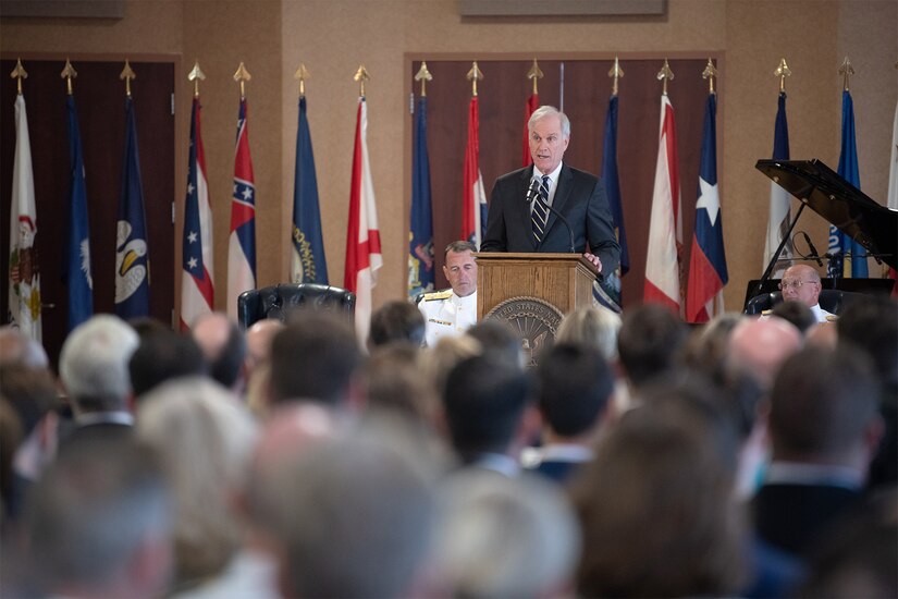 Civilian wearing a suit speaks at a lectern.