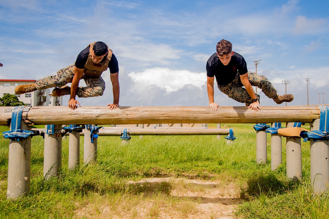 Two Marines jump over an obstacle.