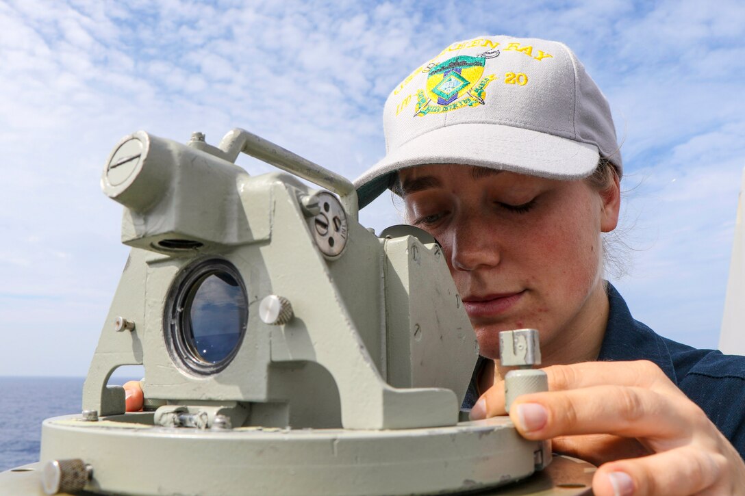 A sailor looks into an alidade on a ship's deck.