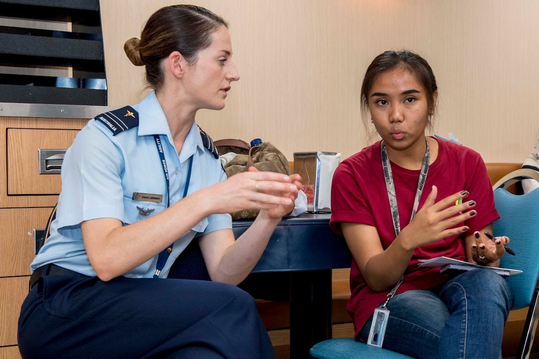 A service member and a civilian talk while sitting in chairs.