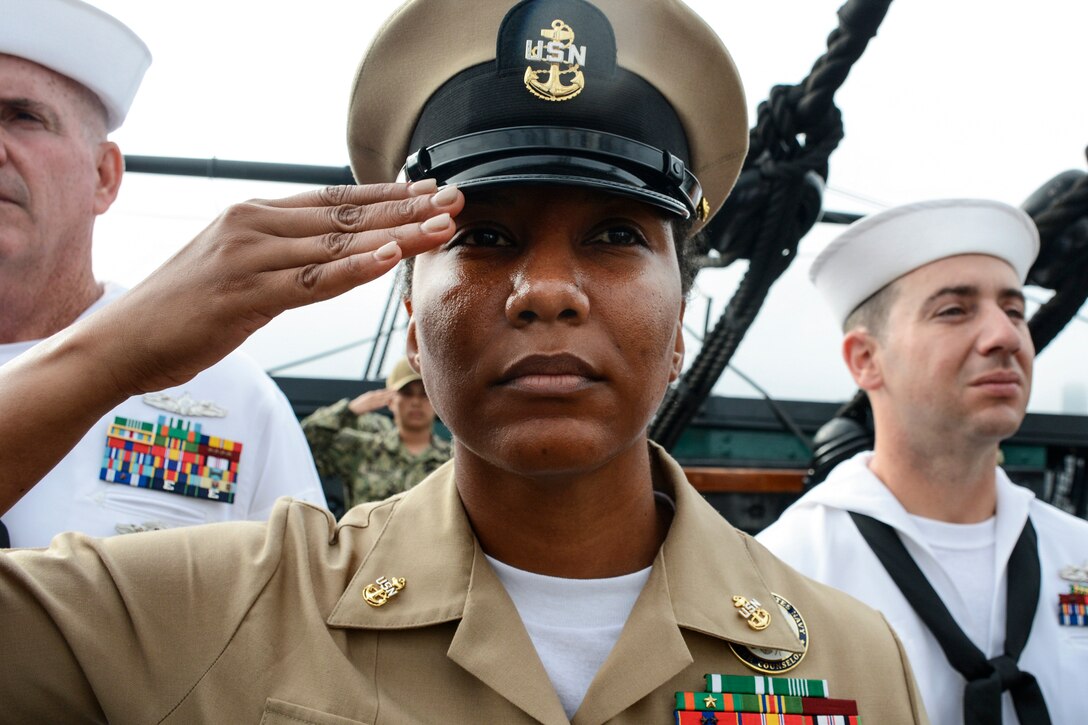 A sailor salutes as two others stand behind her.