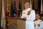 Admiral in white dress uniform speaks at a lectern.