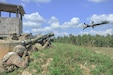 A soldier lays on a grassy hill and fires a rocket.