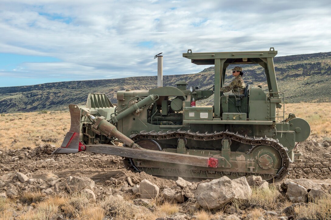 A service member operates a large construction vehicle  on rocky terrain.