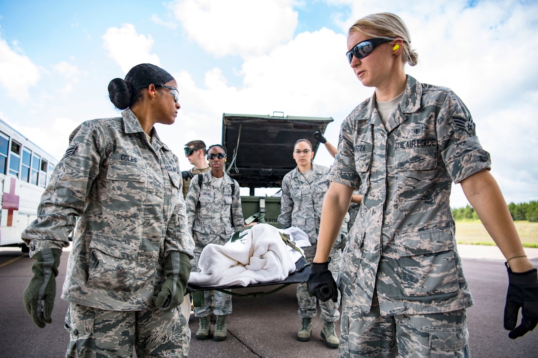 Several airmen carry a stretcher on pavement.