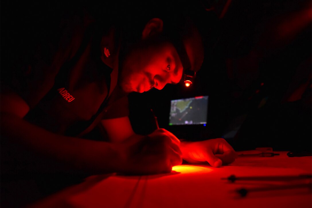 A service members writes on a chart in the dark.