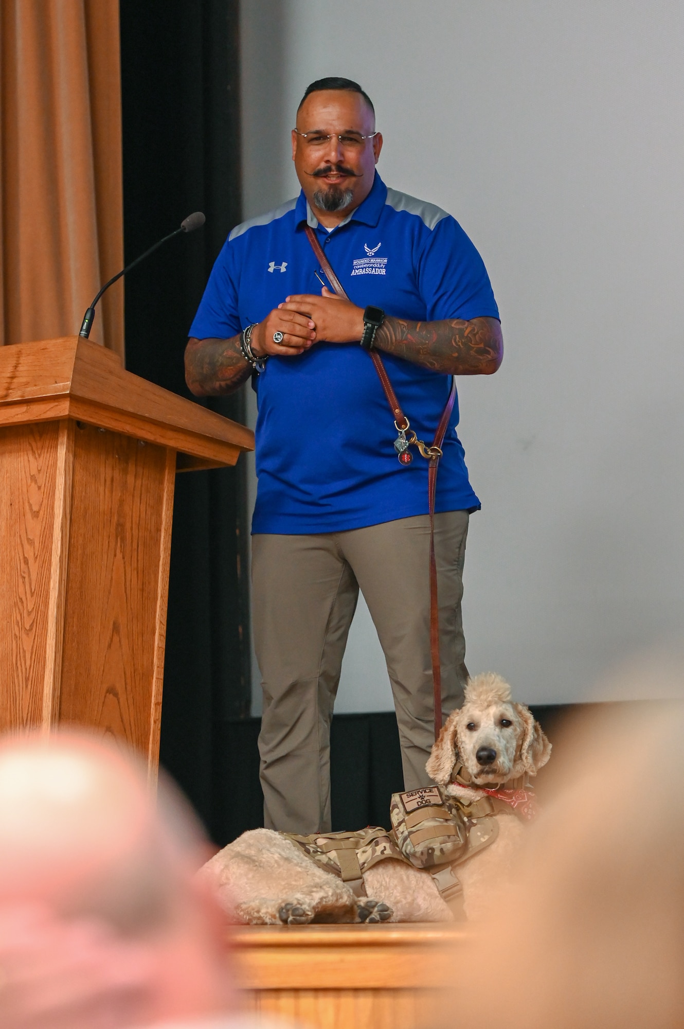Master Sgt. Jose Rijos, senior noncommissioned officer in charge of domestic operations, Massachusetts Air National Guard and Wounded Warrior Ambassador, accompanied by his service dog, Cairo, speaks at the Hanscom Air Force Base theater, Aug. 22. As an Air Force Wounded Warrior Program ambassador, Rijos shared his personal story of post-traumatic stress disorder and the steps he took to recovery. (U.S. Air Force photo by Mark Herlihy)