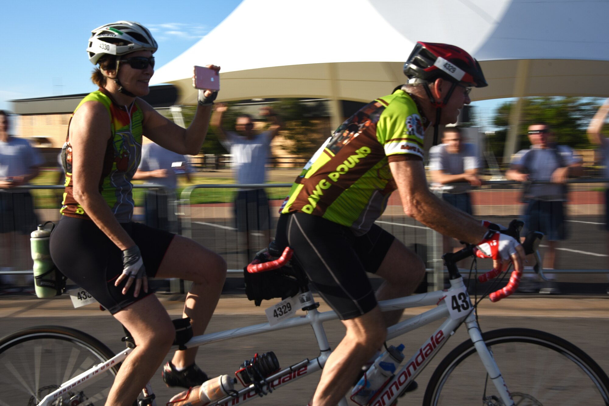 Hotter‘N Hell Hundred cyclists ride a tandem bicycle and take photos of the Airmen cheering for them as they cruise down Airmen’s Alley at Sheppard Air Force Base, Texas