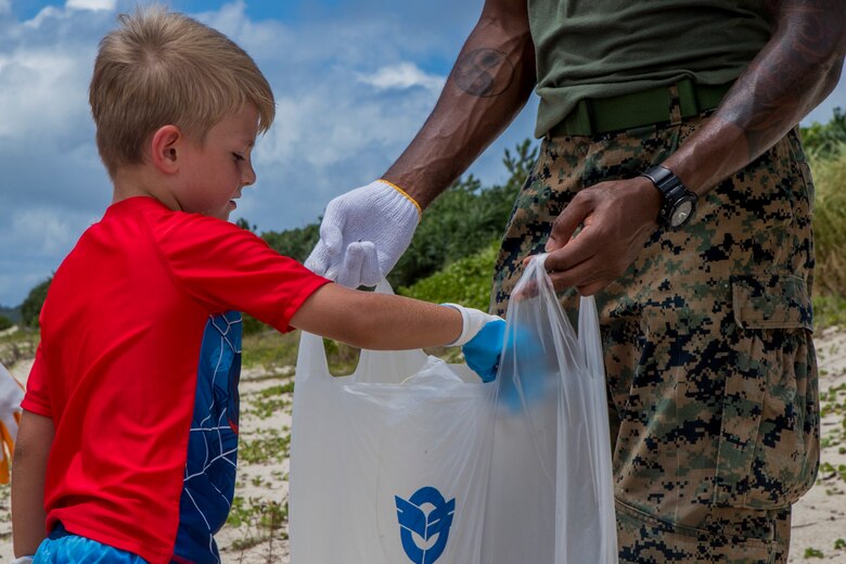 伊芸ビーチでのゴミ拾いに参加した児童が拾ったゴミをゴミ袋に入れるところ。アメリカ海兵隊員の家族の児童２５人と6人の引率の大人が伊芸ビーチで清掃活動を行いました。
