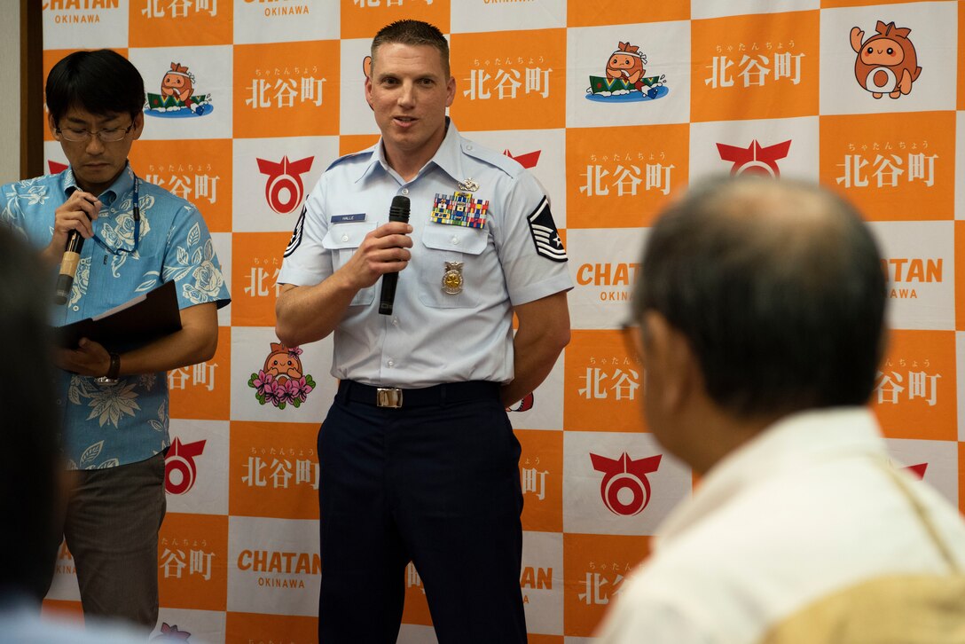 Two men talk into microphones, while a man sits and listens.