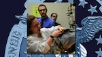 Sara Beth Erpel performs a leak test on military clothing in a lab with two other people looking on.