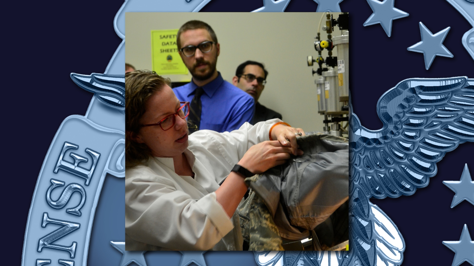 Sara Beth Erpel performs a leak test on military clothing in a lab with two other people looking on.